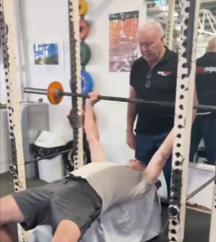 A trainer at Supershape Gym demonstrating proper form to a gym member on a bench press, emphasizing the Precision Training concept.